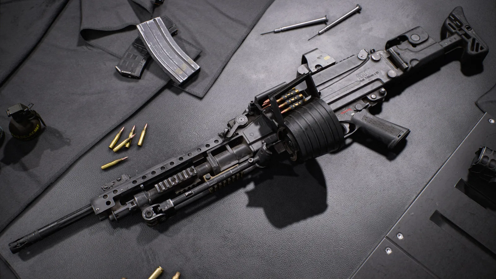 The M121 A2 belt-fed machine gun lying on a dark workbench with its drum, loose cartridges, magazines and tools