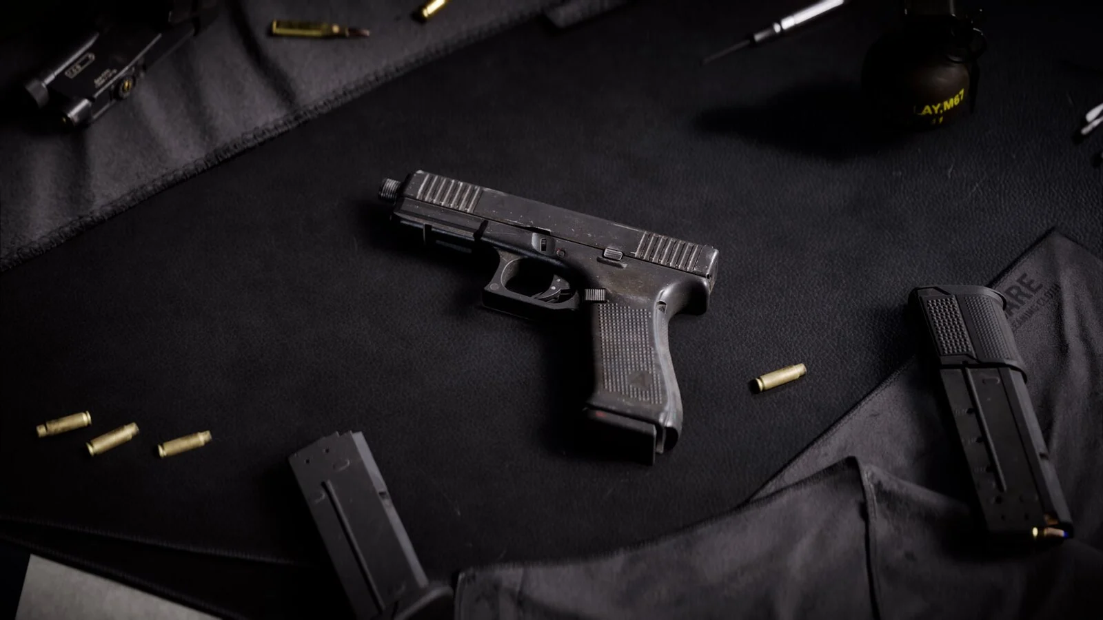 The GGH-22 pistol lying on a black gun mat with two spare magazines, loose cartridge cases and a grenade