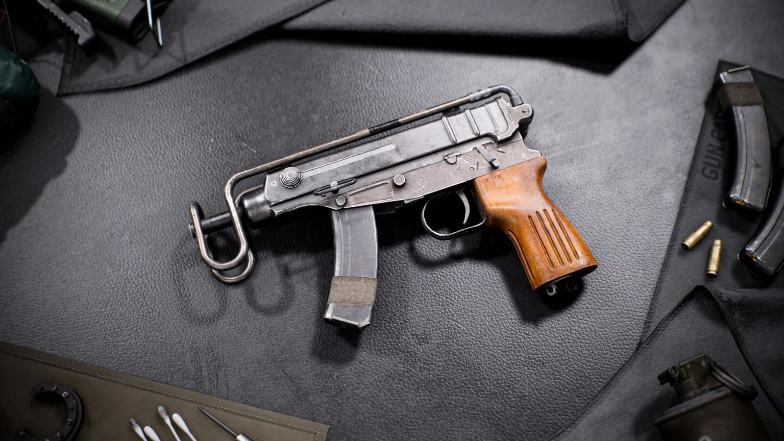 The vz. 61 machine pistol with a wooden grip, folded wire stock and curved magazine lying on a dark gun mat next to spare magazines and cartridges