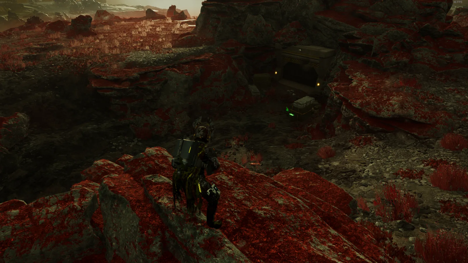 A Helldiver on a red rocky ridge looking down at a bunker door with a supply crate beside it