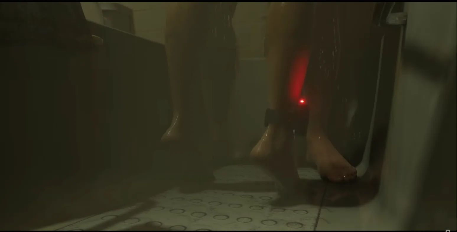 Low shot of bare feet on a shower floor, with a black strap device and a red light on one ankle